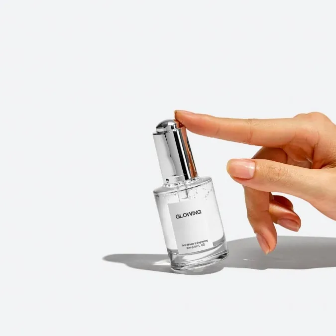 Hand pressing the atomizer of a glass perfume bottle